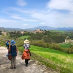 View of people walking downhill into a valley and looking across to a castle on a hill